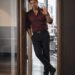 Dark-haired man in a burgundy shirt leaning in an office doorway and raising one hand