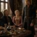 Blonde woman seated at a banquet table with two men in a royal chamber