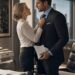 Lucia adjusts Lucas's tie in his office as he holds papers for an important business presentation.