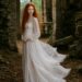 Tess with long red curls in a flowing white dress standing inside ancient castle ruins