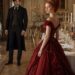 Tess in a red evening gown with Aiden behind her in an elegant candlelit dining room