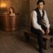 Tess sitting in a large copper bathtub while Aiden waits nearby on a wooden bench