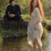 Smiling Tess wading barefoot through a shallow stream while Aiden watches from the bank