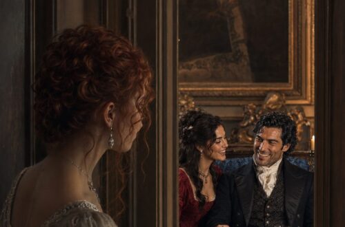 Tess watching from a doorway as Aiden laughs with an elegant dark-haired woman in red