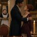 Aiden gripping a red-haired woman's shoulders as a shocked maid enters the dining room