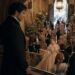 Aiden watching Viktoria from an upper staircase as she mingles with guests at a grand ball