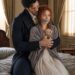 Aiden holding bound and gagged Tess on a bed as she sits wrapped in a gray cloak