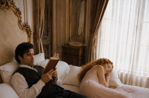 Aiden reading on the bed while Tess sleeps peacefully beside him in a soft pink nightgown